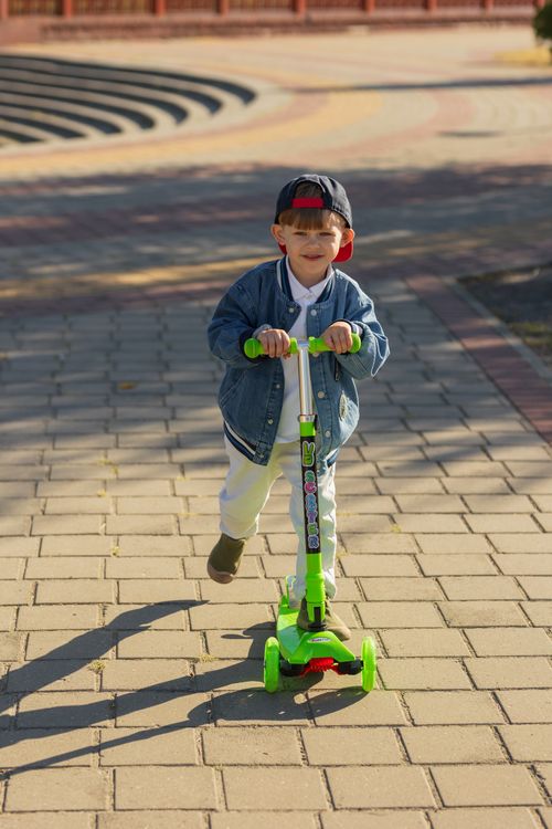 Free Smiling boy in casual wear riding a green scooter on a sunny day. Stock Photo