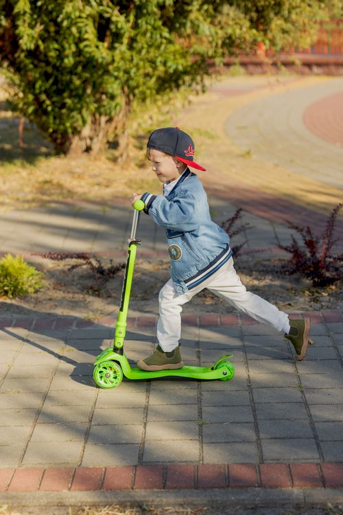 Free A young boy enjoys a sunny day by riding his green scooter in the park. Stock Photo