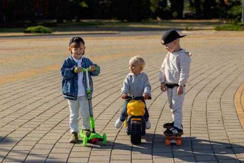 Free Three children playing on scooters and trike in sunny park. Stock Photo