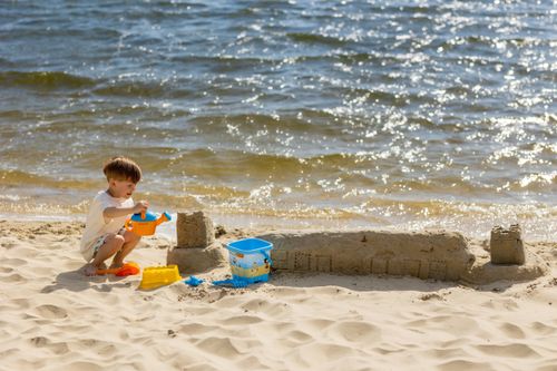 Free A young boy builds a sandcastle on a sunny beach by the lakeside. Stock Photo