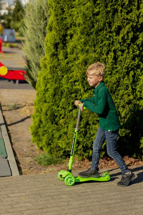 Free Blonde boy riding a green scooter on a sunny day in a park. Stock Photo