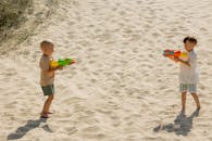 Boys Playfully Shooting Water Guns on Sandy Beach