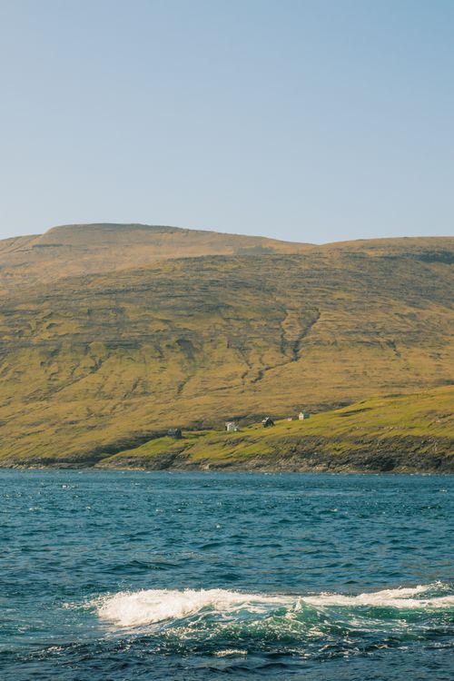 Free Serene coastal view of the Faroe Islands with distant green hills under a clear sky. Stock Photo