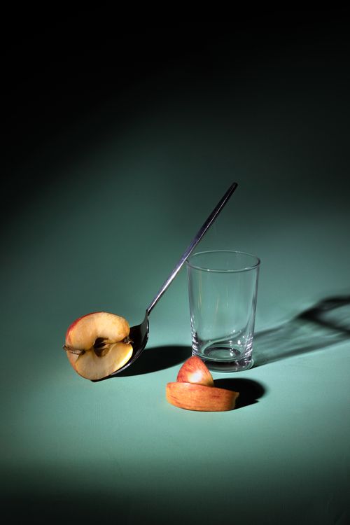 Free Minimalist still life of a sliced apple, glass, and spoon on green background. Stock Photo