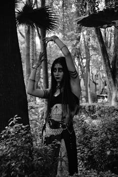 Black and white portrait of a gothic woman posing in a mysterious forest setting.