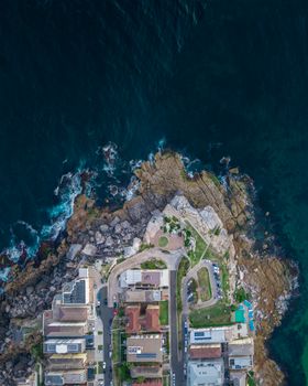 Drone shot of a coastal town with buildings near the rocky shoreline adjacent to the ocean.