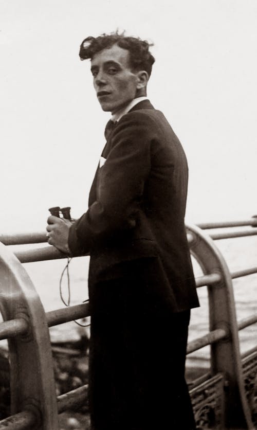 Grayscale Photo of Man Standing By the Railings With Binoculars