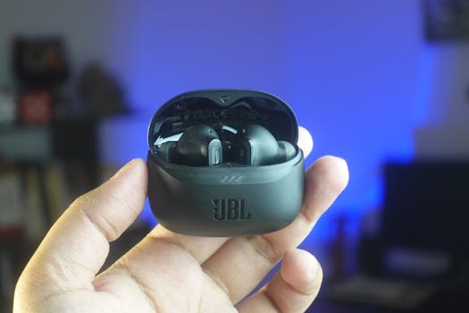 High-quality close-up of hand holding JBL wireless earbuds indoors with cozy background lighting.