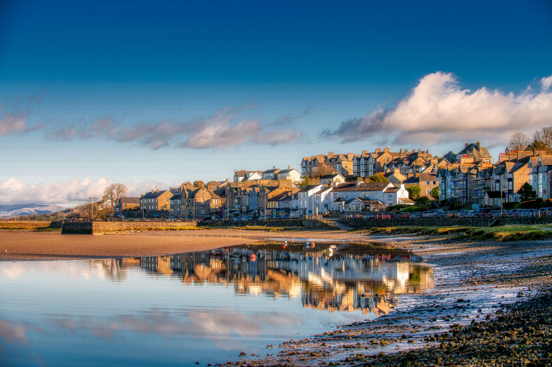 Charming village of Arnside, England, reflected in calm waters under a vibrant sky.