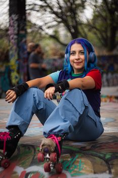 Vibrant portrait of a young woman with blue hair roller skating in a graffiti-covered park.