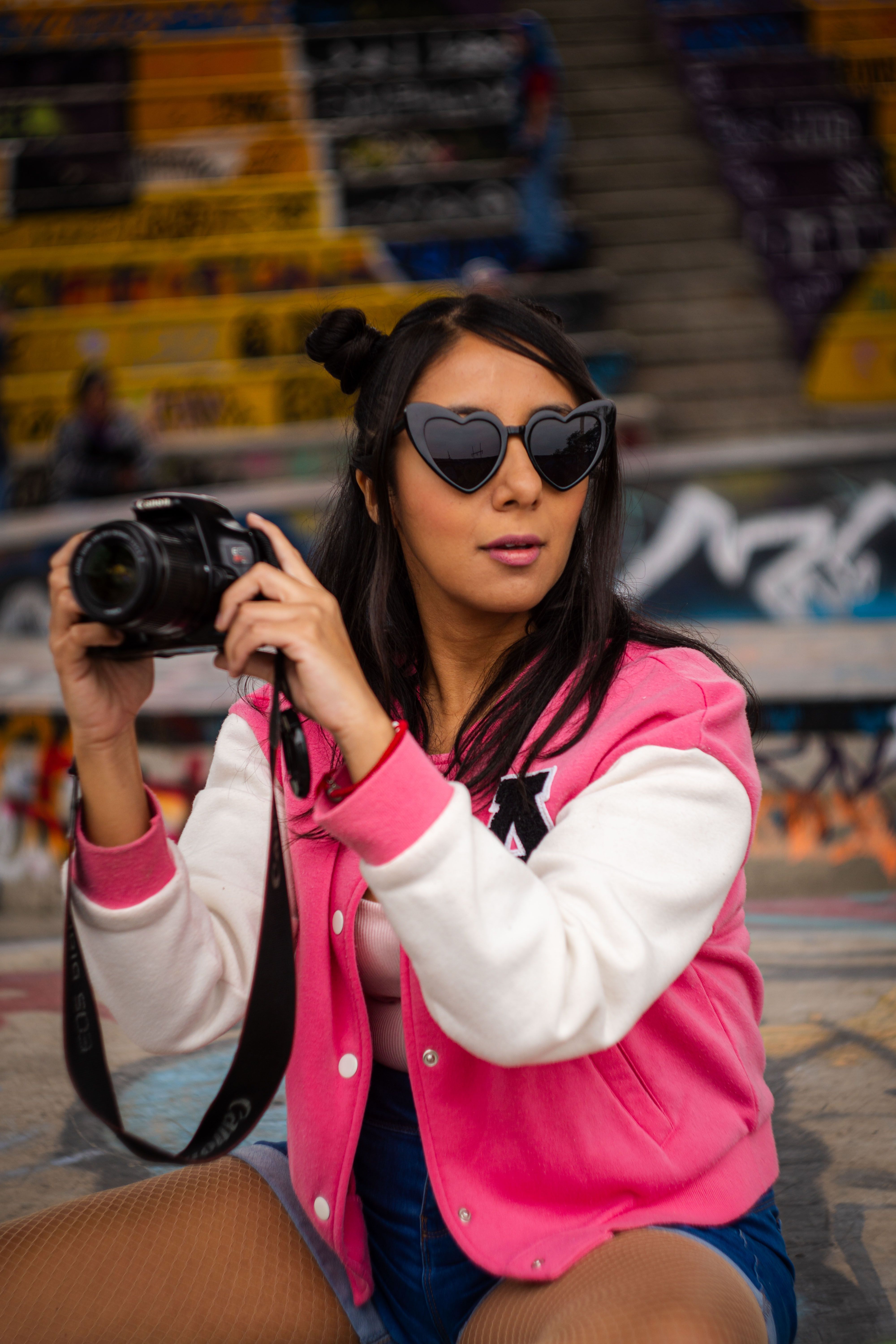 Young woman with heart sunglasses capturing urban art in trendy outfit