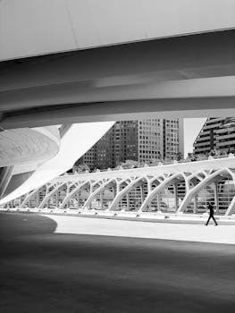 Black and white photo of a person walking under modern structures at Valencia's City of Arts and Sciences.