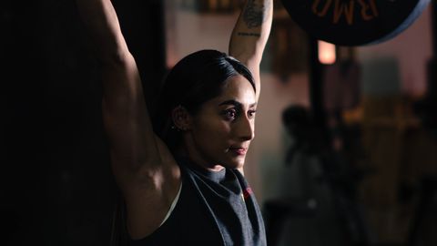 Focused woman lifting a barbell during strength training in a gym environment.