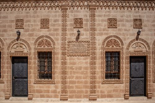 Free Detail of a traditional stone facade in Mardin showcasing intricate carved designs and iron doors. Stock Photo