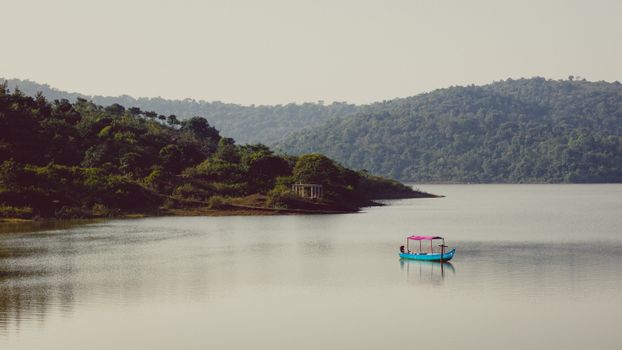 Peaceful landscape with a boat on a tranquil lake surrounded by hills in Koraput, India.