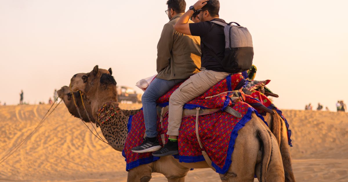 Two people enjoy a colorful camel ride through a desert landscape during sunset.