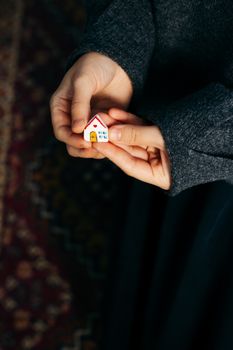 Close-up of hands holding a small toy house on patterned fabric, symbolizing home.