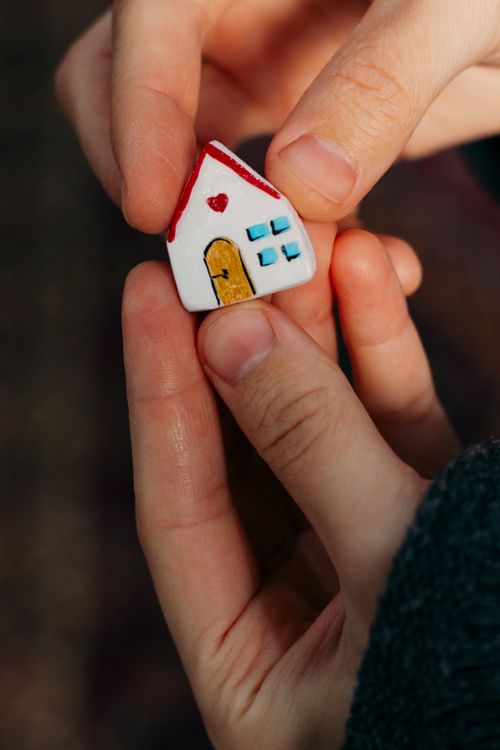 Free Close-up of hands holding a small handmade house figurine symbolizing home and family. Stock Photo