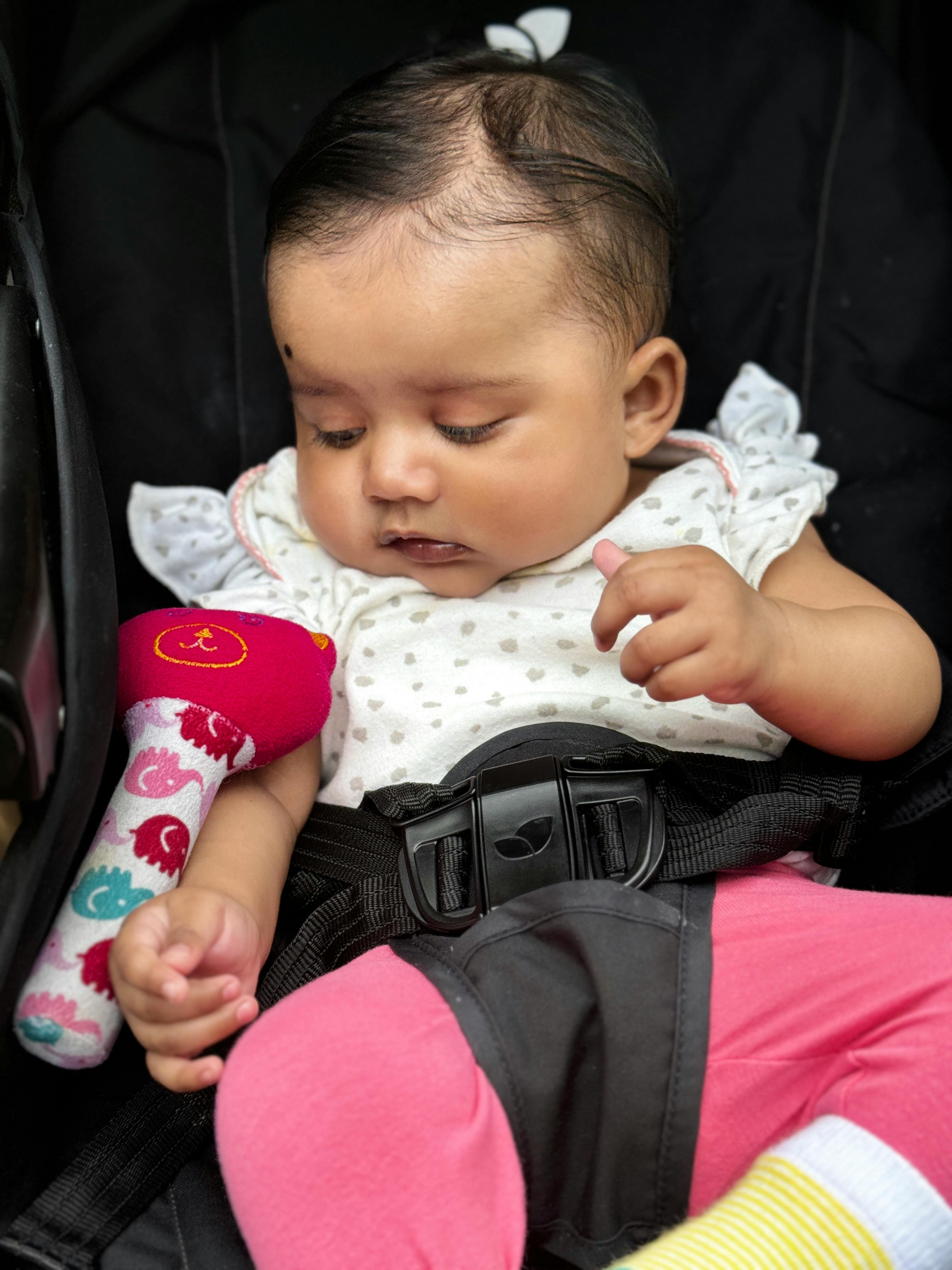 A cute baby in a stroller, captivated by a colorful toy in a cozy setting.