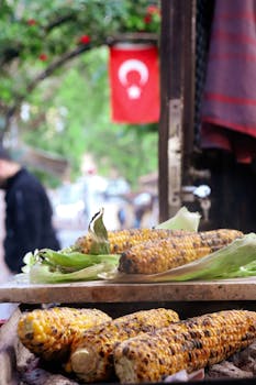 Grilled corn on display in a vibrant Turkish street market with a national flag.