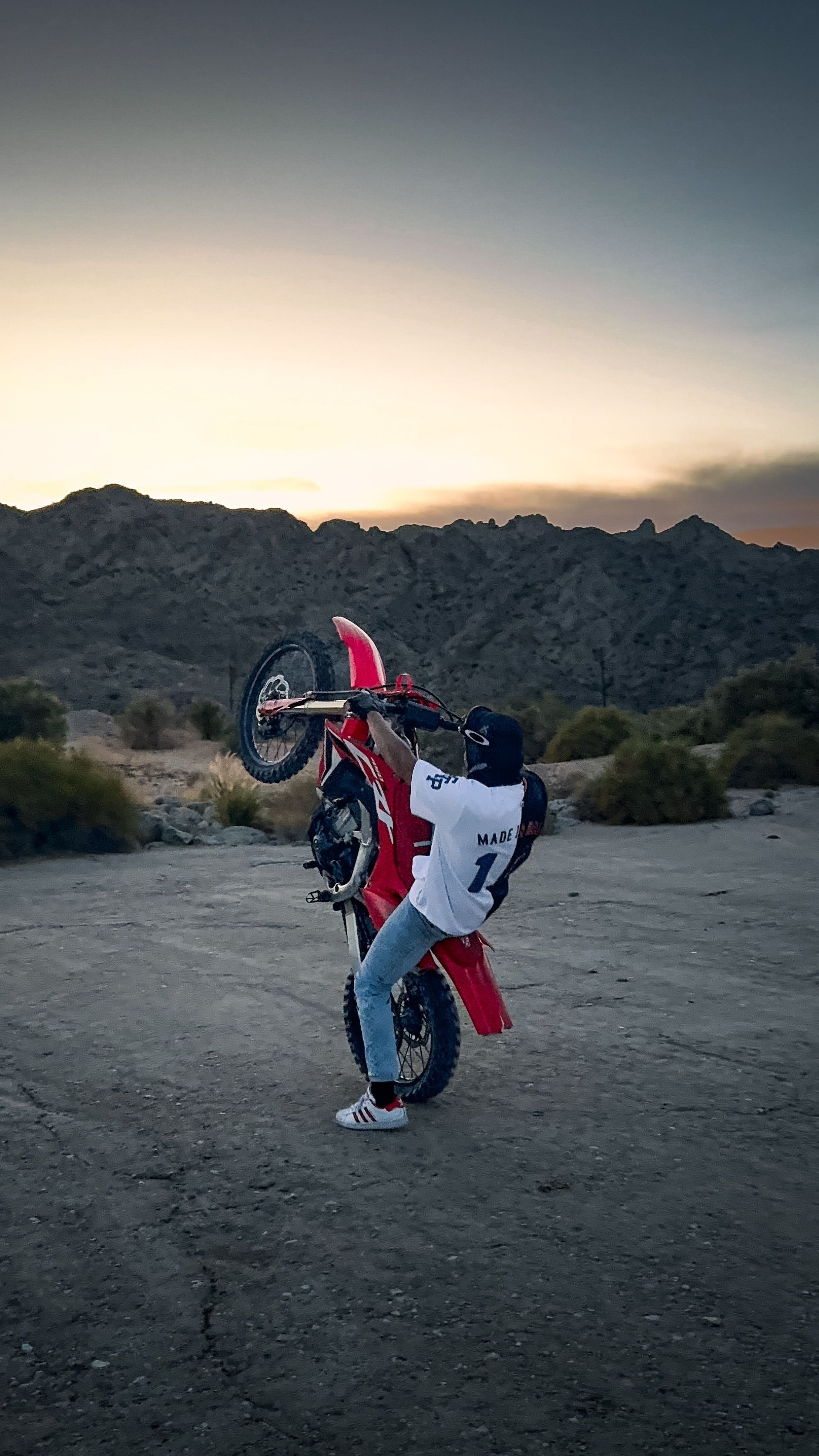 A motorcyclist performs a wheelie against a mountainous sunset backdrop.