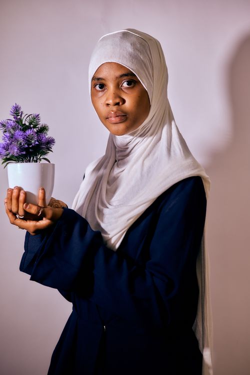 Free A woman in a hijab holding a potted plant, captured in a studio setting, emphasizing serenity and elegance. Stock Photo
