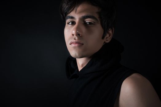 Artistic portrait of a young man wearing a black hoodie against a dark background.