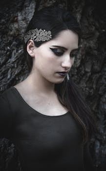 Close-up portrait of a woman with intricate hairpiece and bold makeup against a textured background.