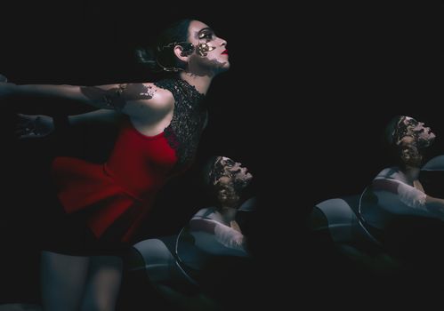 A striking artistic portrait of a woman in a red dress with creative face paint against a dark background.