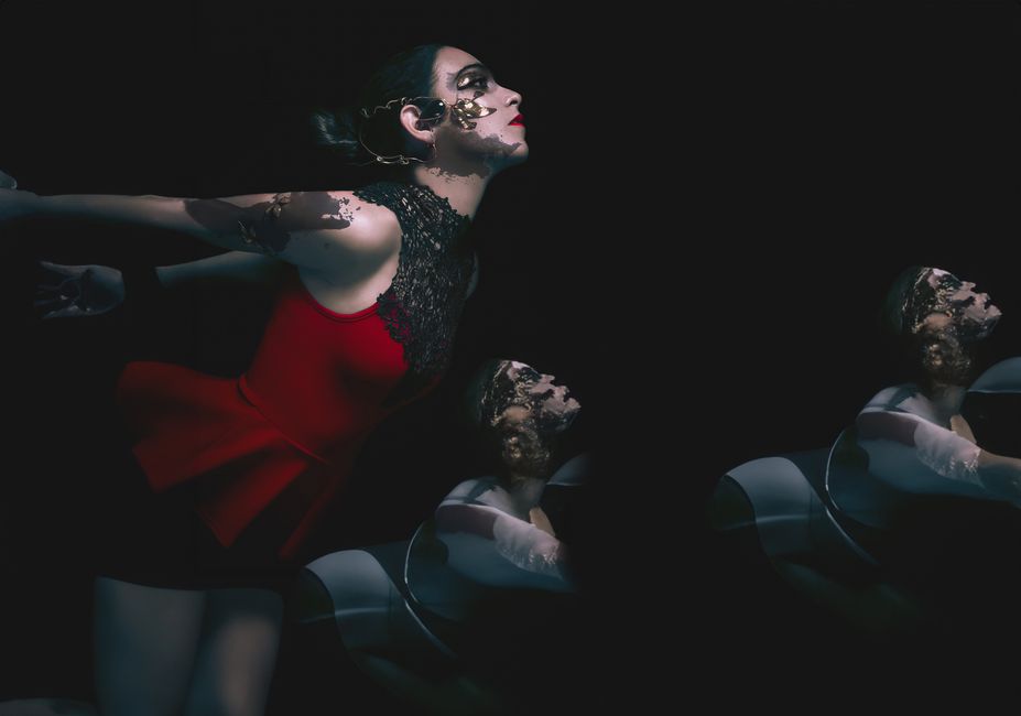 A striking artistic portrait of a woman in a red dress with creative face paint against a dark background.