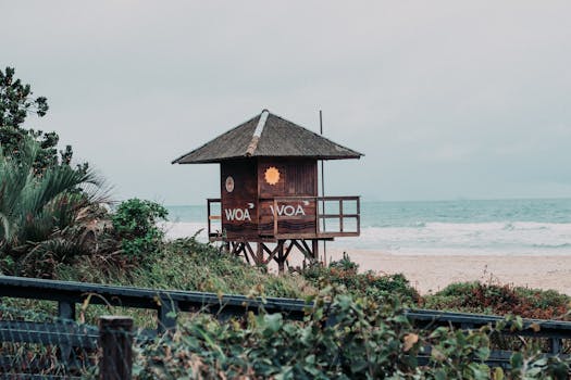 A rustic wooden lifeguard hut overlooking a serene ocean beach under a cloudy sky.