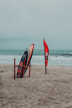 Colorful surfboards and kite on a sandy beach with ocean waves in the background.