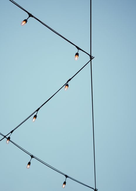 Diagonal string lights against a clear blue sky create a minimalist geometric pattern.