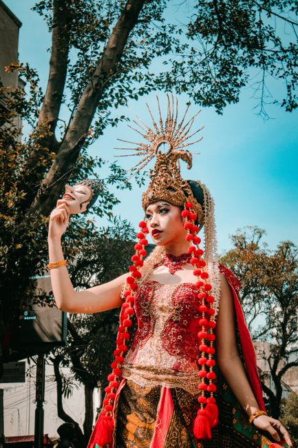 Beautiful Indonesian dancer in traditional costume outdoors with elaborate headdress.