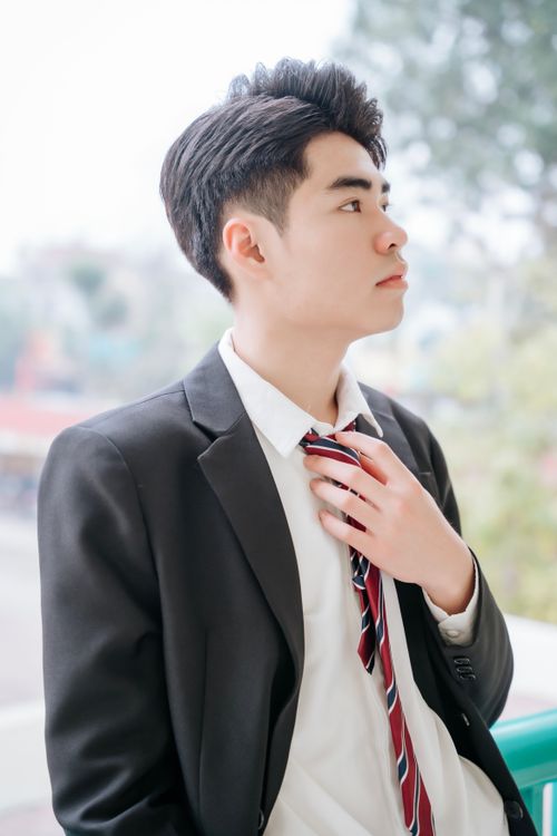 Free Young adult in formal attire adjusting tie, looking thoughtful and professional outdoors. Stock Photo