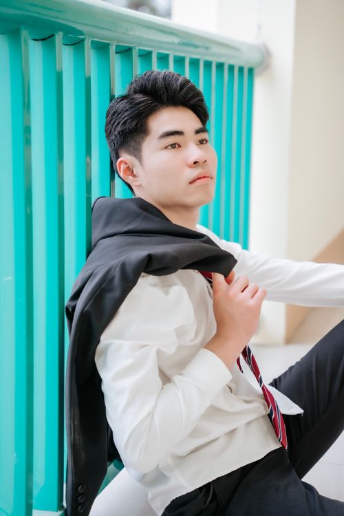 Free Young Asian adult in formal wear with jacket draped over shoulder, posing indoors. Stock Photo