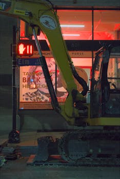 Yellow construction tractor at night in urban setting with neon lights.