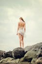 日落时分，一名女子穿着比基尼，站在海滩边的岩石上，享受着夏日的微风