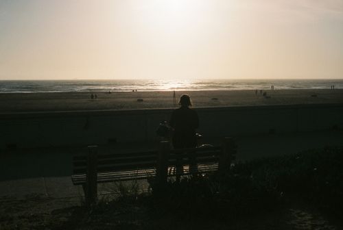 Free A lone figure on a bench gazes at the sunset over the ocean, creating a serene silhouette. Stock Photo