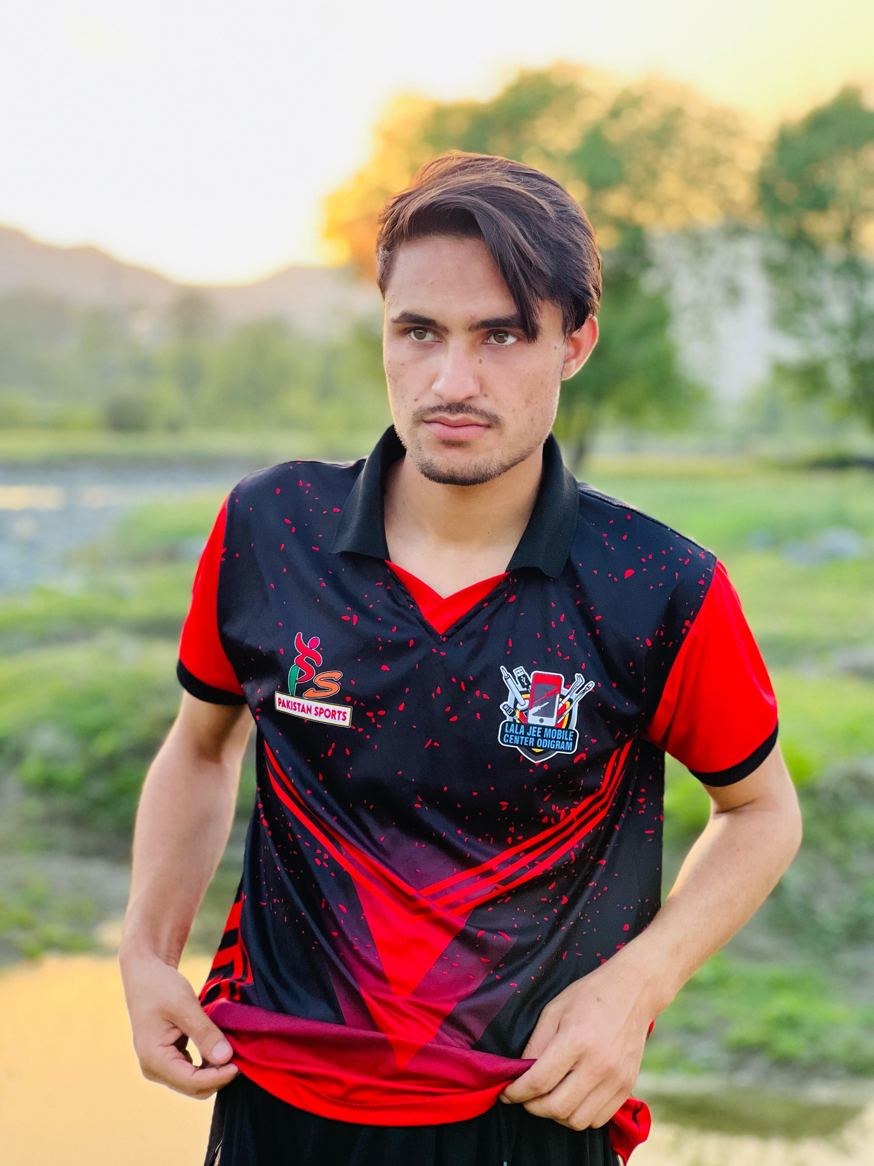 Portrait of a young man in a sports jersey standing outdoors at sunset, with vibrant colors.