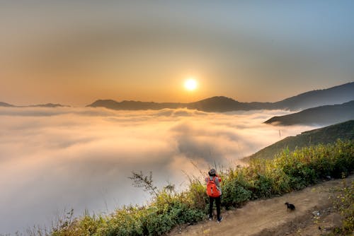 Person Wearing Red Backpack Facing Sea of Clouds