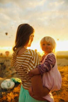 A mother and child at sunrise in Cappadocia with hot air balloons in the background.