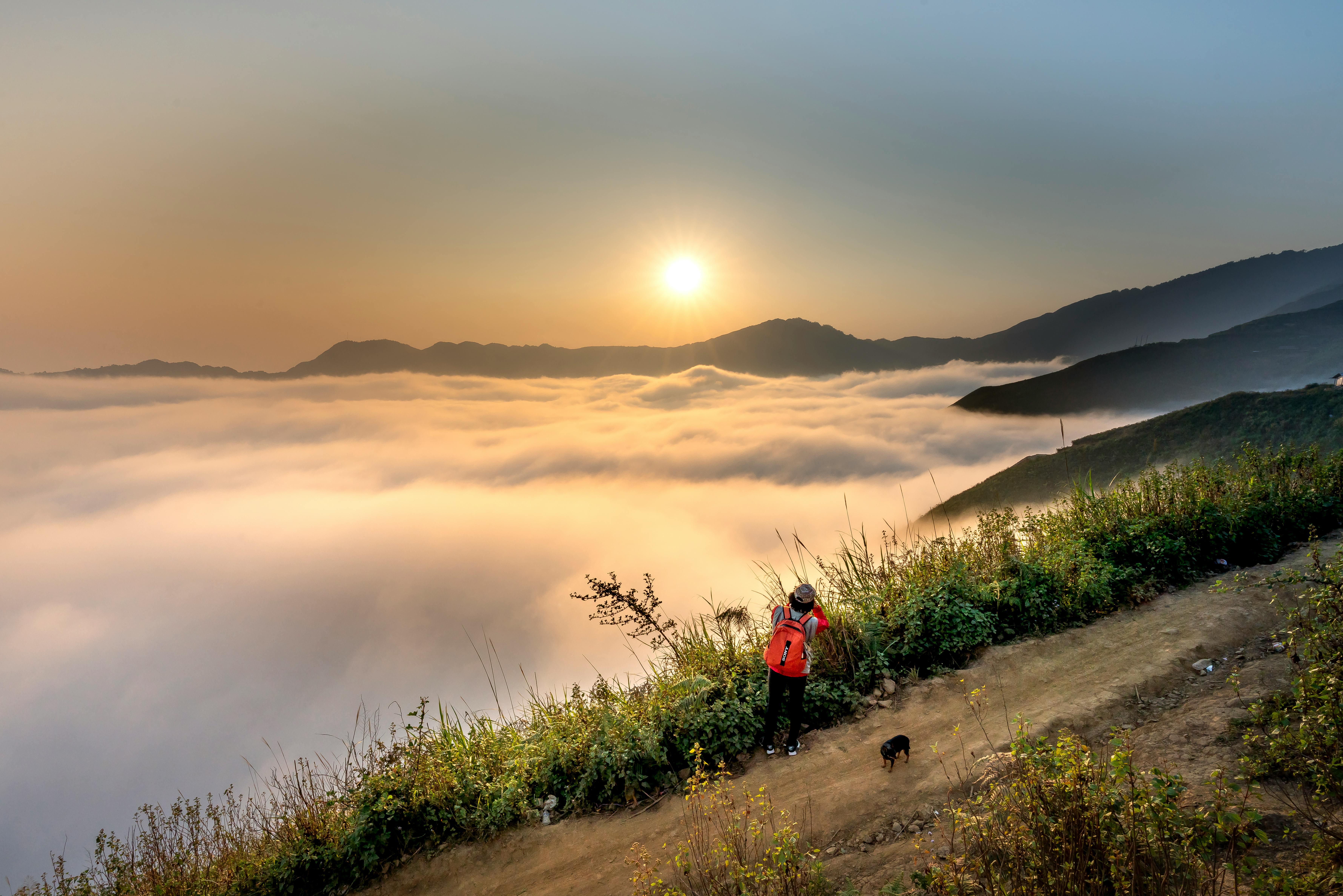 一位背着红色背包的徒步旅行者，在山谷和云海之上欣赏着令人惊叹的日出