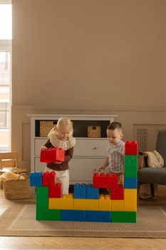 Two children building a colorful wall with big blocks indoors.