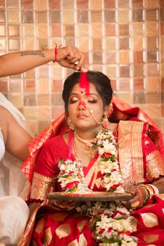 A bride in a red sari participates in a traditional Indian wedding ritual, showcasing cultural richness.