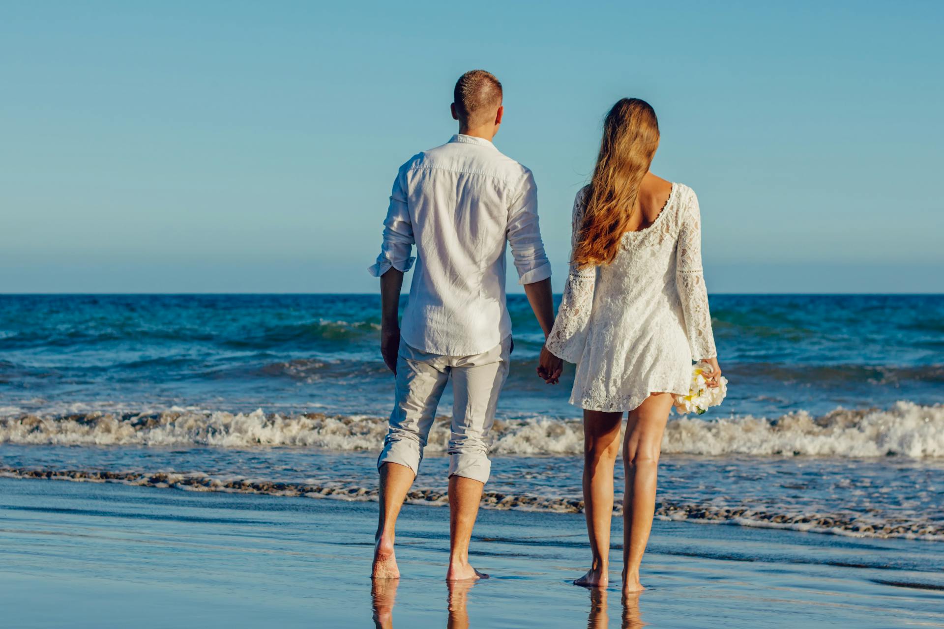 A couple enjoying a romantic walk along the seashore, holding hands and barefoot on the sand.