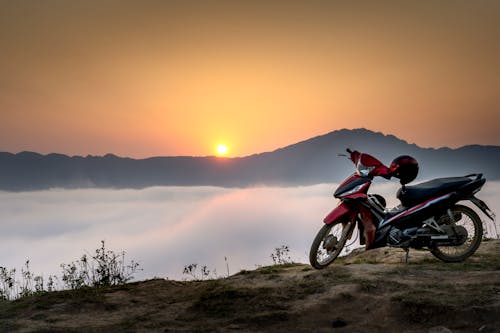 красный и черный мотоцикл Underbone на горном утесе, окруженном морем облаков