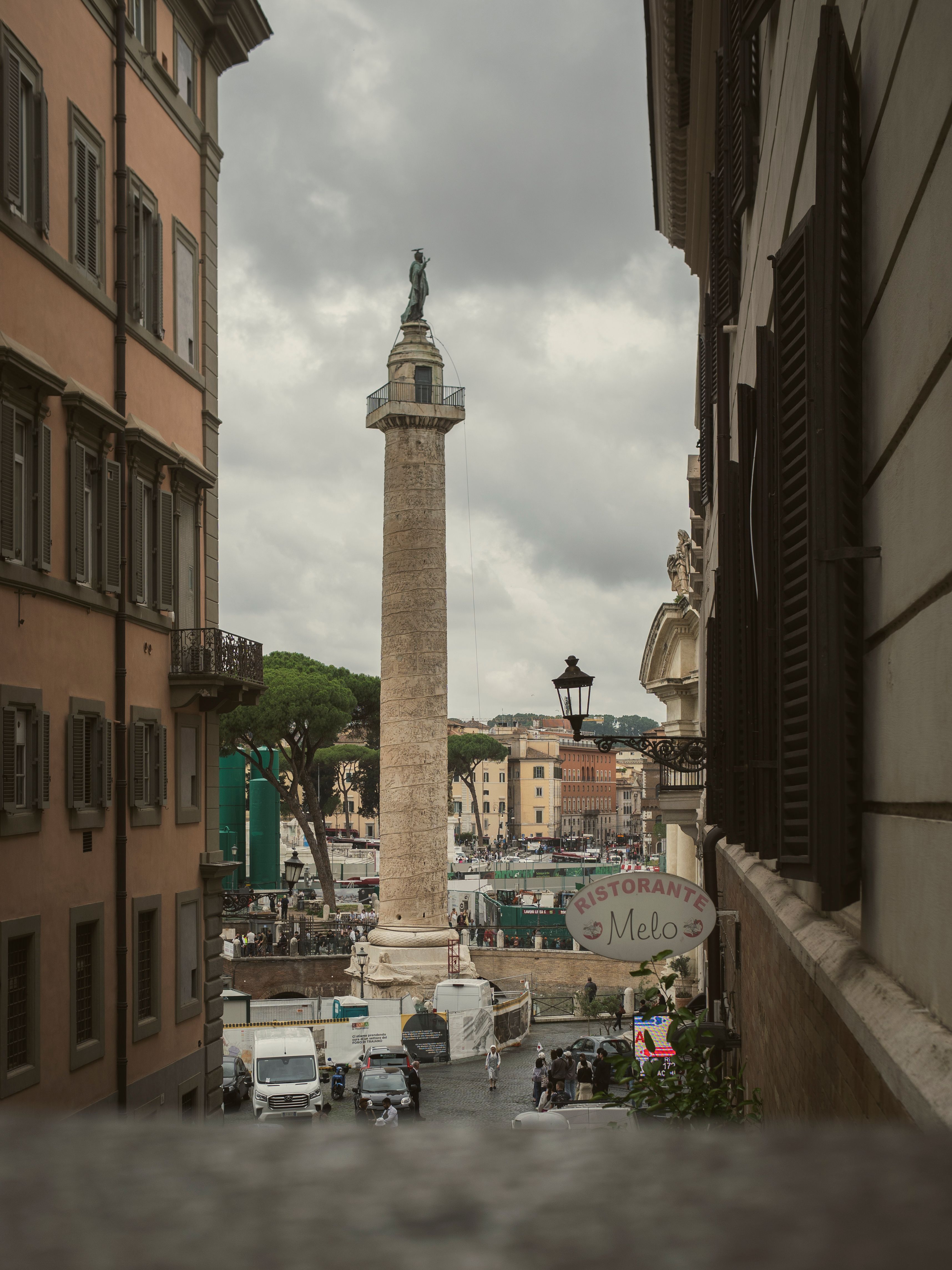 Scenic view of Trajan's Column in Rome, framed by historic buildings under cloudy skies.
