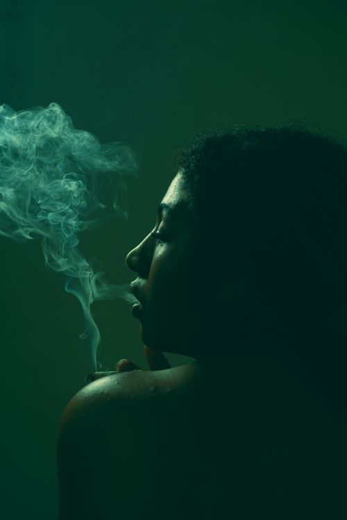 Free Dramatic portrait of a woman exhaling smoke in low light with a mysterious, moody ambiance. Stock Photo