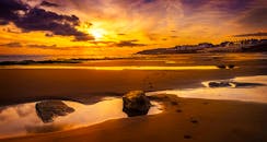 宁静的海滩上，金色的日落映在沙滩倒影中，远处是海岸线的建筑